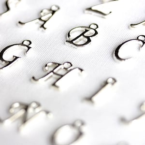 May include: A collection of silver letter charms, each letter is individually crafted and has a delicate, cursive style.
