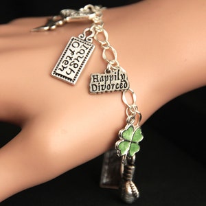 May include: Silver charm bracelet with multiple charms, including a charm with the text "Happily Divorced" and a green shamrock charm.