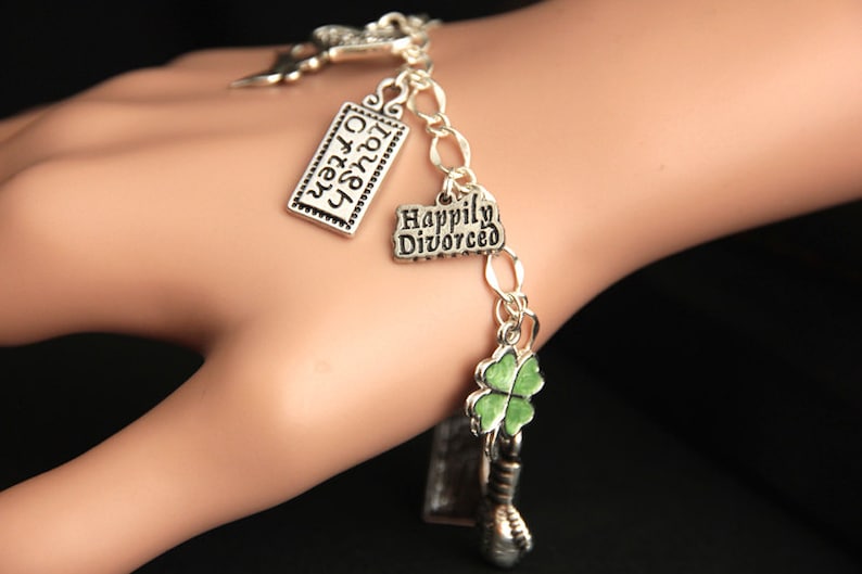 May include: Silver charm bracelet with multiple charms, including a charm with the text "Happily Divorced" and a green shamrock charm.