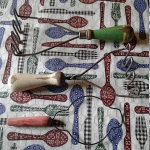May include: Three vintage potato mashers with wooden handles. The handles are painted in different colors: green, white, and pink. The mashers are made of metal wire.