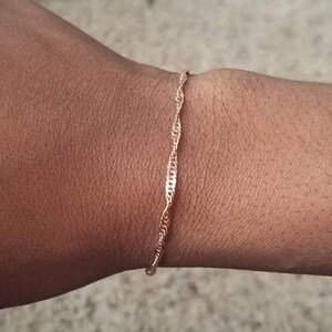 woman wearing a small, thin rose gold plated Singapore chain bracelet, a curb chain that twists on itself.
