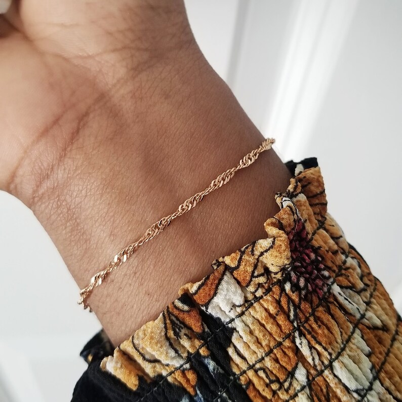 woman wearing a small, thin rose gold plated Singapore chain bracelet, a curb chain that twists on itself.