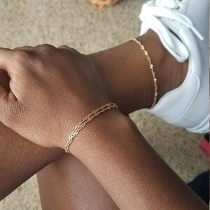 woman wearing a small, thin rose gold plated Singapore chain double bracelet, a curb chain that twists on itself, and a matching anklet.