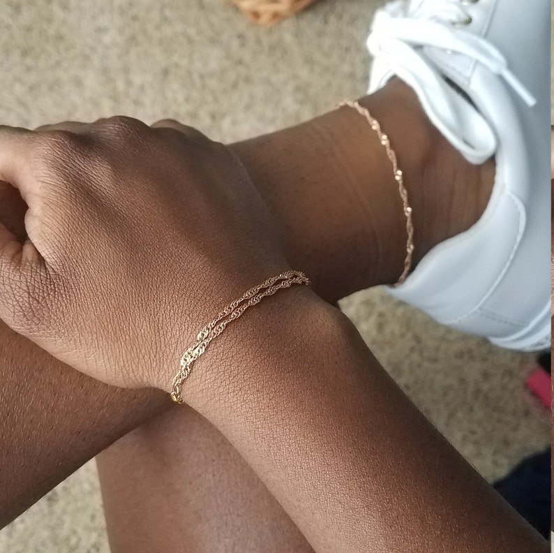 woman wearing a small, thin rose gold plated Singapore chain double bracelet, a curb chain that twists on itself, and a matching anklet.