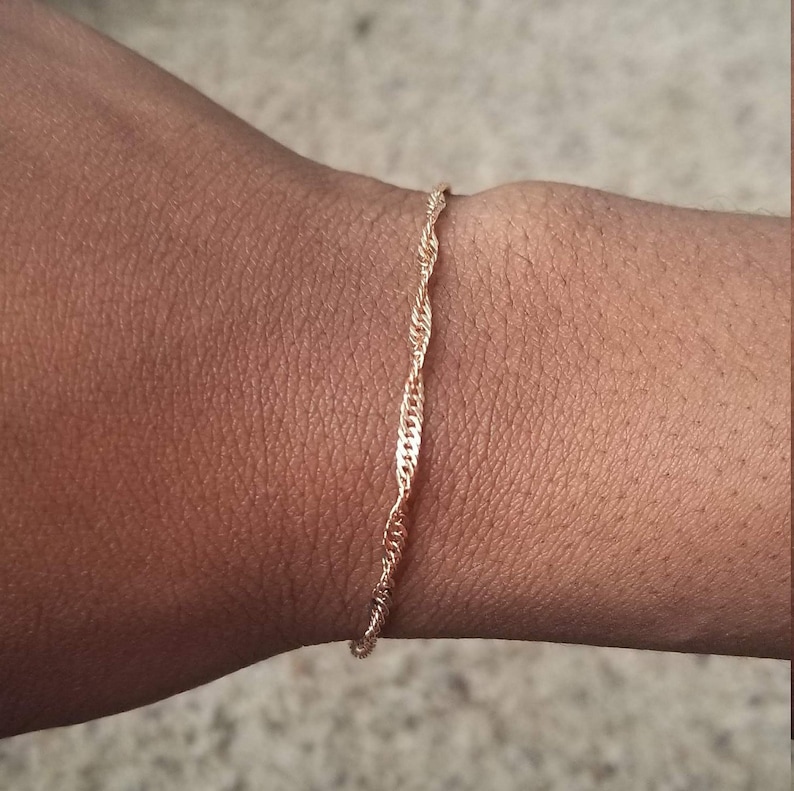 woman wearing a small, thin rose gold plated Singapore chain bracelet, a curb chain that twists on itself.