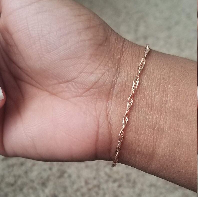 woman wearing a small, thin rose gold plated Singapore chain bracelet, a curb chain that twists on itself.