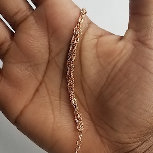 double Singapore chain bracelet, a curb chain that twists on itself, in a woman's hand.