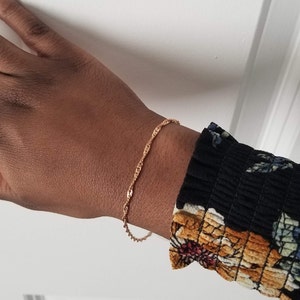 woman wearing a small, thin rose gold plated Singapore chain bracelet, a curb chain that twists on itself.