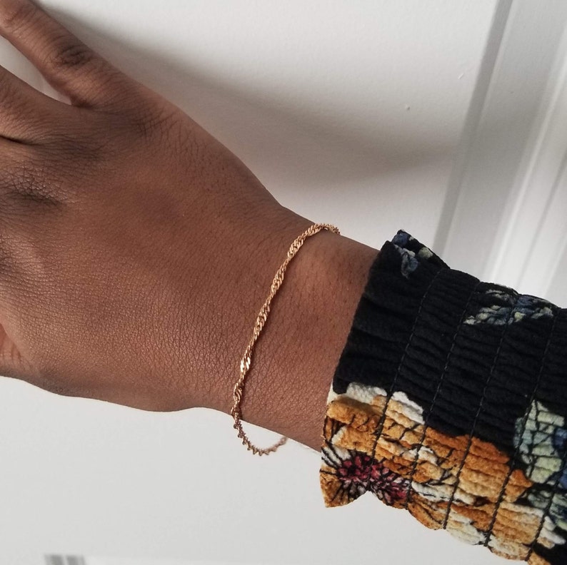 woman wearing a small, thin rose gold plated Singapore chain bracelet, a curb chain that twists on itself.