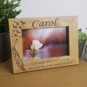 May include: A wooden photo frame with a white rose and a sunset in the background. The frame is engraved with the text "Carol" and "Loved beyond words, missed beyond measure".