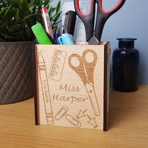 Könnte beinhalten: Ein hölzerner Stiftehalter mit einer personalisierten Inschrift, die "Miss Harper" lautet, und einem Design aus Schulutensilien wie Lineal, Schere, Buntstiften, Büroklammern und Reißnägeln. Der Halter ist mit Stiften, Bleistiften und einer Schere gefüllt.