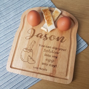 Può includere: Un tagliere per la colazione in legno a forma di fetta di pane tostato con due incavi per le uova, due fessure per i soldati e un messaggio personalizzato che recita "Jason Puoi intingere il tuo Soldato nel mio uovo in qualsiasi giorno! Con affetto Natalie".
