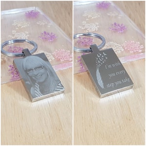 May include: A silver keyring with a photo of a woman on one side and the words "I'm with you every step you take" on the other side. The keyring has a feather and flying birds engraved on the side with the text.