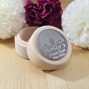 Può includere: Una scatola di legno con un coperchio argentato inciso con un arcobaleno, nuvole e il testo "Holly's First Curl May 2023".