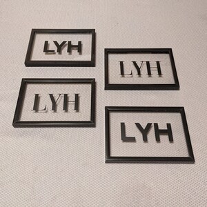 May include: Four black picture frames with clear glass fronts. Each frame displays the letters "LYH" in black.