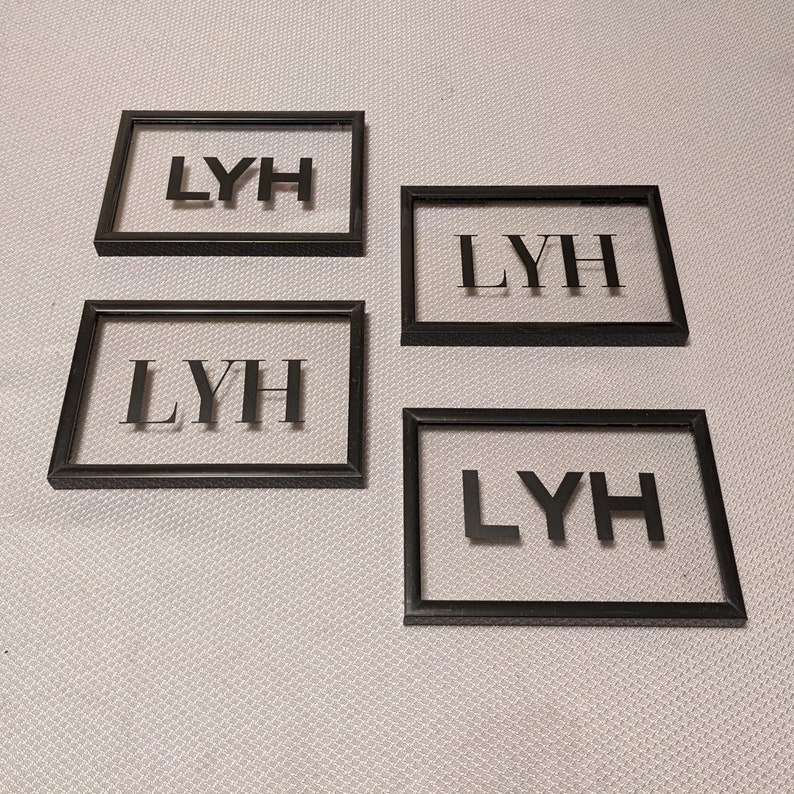 May include: Four black picture frames with clear glass fronts. Each frame displays the letters "LYH" in black.