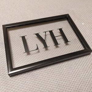 May include: A black framed picture with a clear glass insert. The word "LYH" is printed in black on the glass.