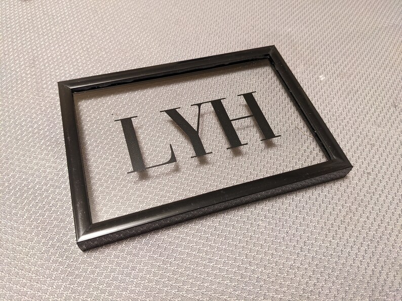 May include: A black framed picture with a clear glass insert. The word "LYH" is printed in black on the glass.