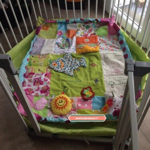 Puede incluir: Una colorida alfombra de juego de patchwork con varios cuadrados de tela, incluyendo patrones florales, de búhos y de peces. La alfombra tiene juguetes adjuntos, incluyendo un sol sonriente y un pez, dentro de una cuna.