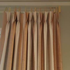 May include: A set of pleated curtains with a beige and brown striped pattern. The curtains are hung on a gold rod.