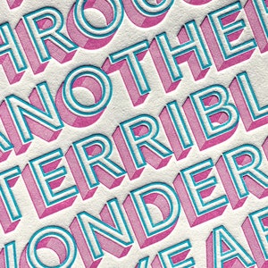 May include: Close-up of a pink and blue graphic design with the text "Through another terrible wonderful year".