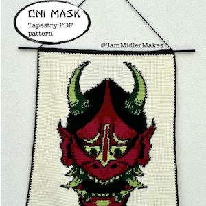 Puede incluir: Un tapiz de ganchillo con un diseño de máscara Oni. La máscara es principalmente roja con detalles en negro, verde y amarillo. El tapiz es rectangular con un fondo blanco y un borde negro. El texto "ONI MASK Tapestry PDF pattern" está en un óvalo blanco.