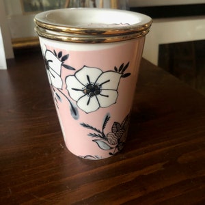 Op de afbeelding: Een roze keramische mok met een gouden rand en een zwart-wit bloemenontwerp.