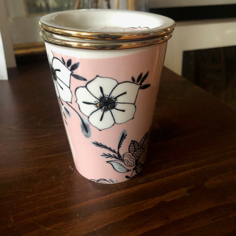 Op de afbeelding: Een roze keramische mok met een gouden rand en een zwart-wit bloemenontwerp.