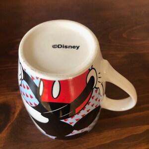 Pu&ograve; includere: Una tazza in ceramica bianca con un design di Topolino nero e rosso. La tazza ha uno sfondo blu con cuori bianchi. Il fondo della tazza dice "&copy;Disney".
