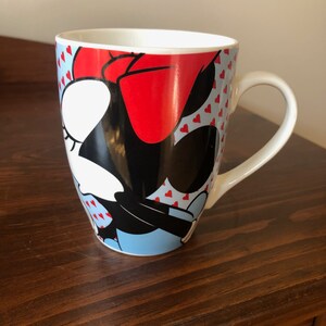 Pu&ograve; includere: Una tazza in ceramica bianca con un'immagine colorata di Minnie Mouse. La tazza ha un fiocco rosso, occhi neri e uno sfondo blu e bianco con cuori rossi.
