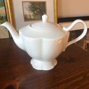 May include: A white porcelain teapot with a fluted body and a lid with a knob. The teapot has a spout and a handle.