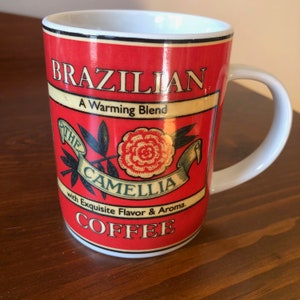 Peut inclure: Une tasse à café en céramique blanche avec un motif rouge, jaune et noir. La tasse porte l'inscription "Brazilian A Warming Blend The Camellia with Exquisite Flavor & Aroma. Coffee".