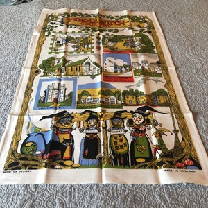 May include: A vintage tea towel with a colorful illustration of Pendle Witch Country, featuring a map of the area with landmarks like Whalley Parish Church and Lancaster Castle. The bottom of the towel shows witches hanging from a tree with a black cat and a cauldron.