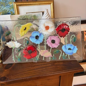May include: A glass serving tray featuring a painted design of colourful flowers. The flowers are red, pink, blue, yellow and white. The tray is clear glass with a slightly textured surface.