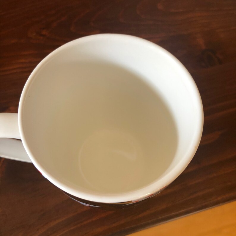 Pu&ograve; includere: Tazza da caff&egrave; in ceramica bianca con manico. La tazza &egrave; vuota e si trova su una superficie di legno.