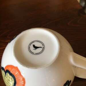 Pu&ograve; includere: Tazza in ceramica bianca con una silhouette di uccello nero e il testo "Dishwasher & Microwave Safe. Made in Indonesia. Fabriqu&eacute; en Indon&eacute;sie." sul fondo.