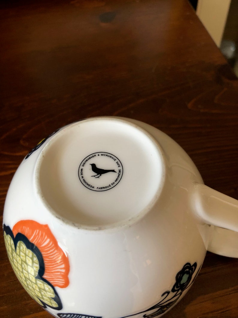 Pu&ograve; includere: Tazza in ceramica bianca con una silhouette di uccello nero e il testo "Dishwasher & Microwave Safe. Made in Indonesia. Fabriqu&eacute; en Indon&eacute;sie." sul fondo.