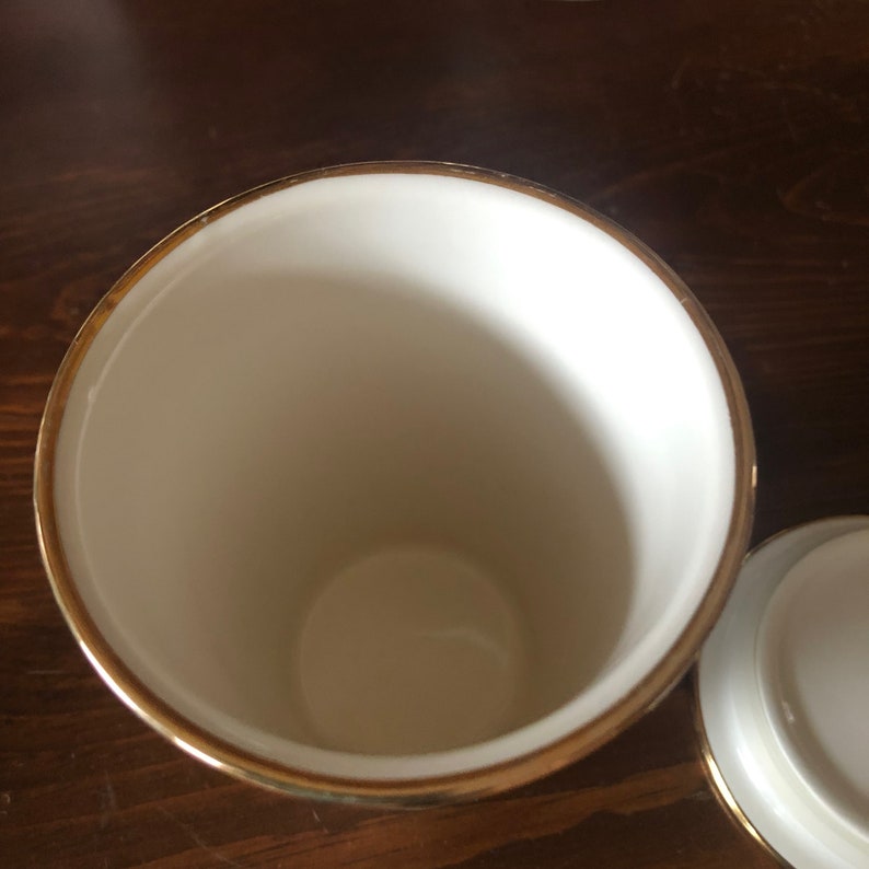 Op de afbeelding: Witte keramische pot met een gouden rand. De pot heeft een deksel.