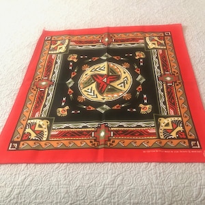 May include: Red bandana with a black and green geometric pattern. The pattern features a central circle with a swirling design and birds on the corners. The bandana is made of 100% cotton and made in the USA.