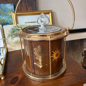 May include: Vintage ice bucket with a brown exterior and gold accents. The cylindrical bucket features a gold handle and trim, with decorative gold designs and a sunburst pattern. The lid and handle are silver.