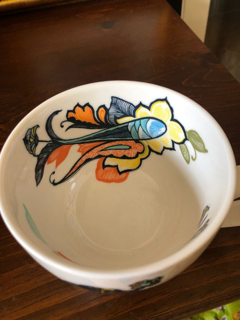 Pu&ograve; includere: Tazza da t&egrave; in ceramica bianca con un design floreale colorato con accenti arancioni, gialli, blu, verdi e neri.