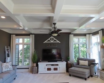 Peut inclure: Un salon avec un plafond blanc avec des poutres apparentes, un mur gris foncé, un meuble TV blanc avec un téléviseur à écran plat, un canapé gris avec des coussins, un fauteuil gris avec un pouf et deux fenêtres avec des rideaux blancs.