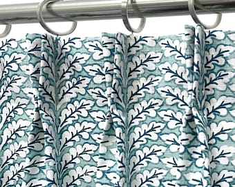 May include: Close-up of a curtain with a repeating leaf pattern in white and teal. The curtain is hanging from a silver rod with silver rings. The fabric is pleated, creating vertical folds.