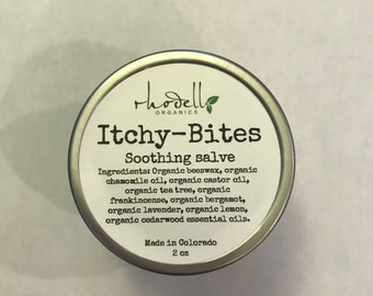 May include: A silver tin with a white label that reads "hodello ORGANICS Itchy-Bites Soothing salve". The label lists the ingredients: Organic beeswax, organic chamomile oil, organic castor oil, organic tea tree, organic frankincense, organic bergamot, organic lavender, organic lemon, organic cedarwood essential oils. The label also states "Made in Colorado 2 oz".