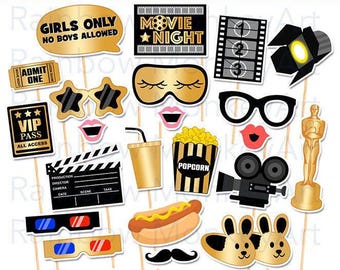 May include: A collection of movie-themed photo booth props on sticks, including a gold speech bubble with text, a film strip, a clapperboard, a popcorn bucket, a hot dog, 3D glasses, a gold statue, a camera, and various masks in black and gold.
