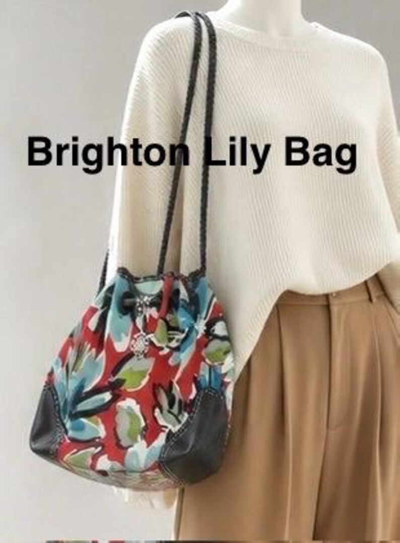 May include: A Brighton Lily Bag featuring a red, blue, and green floral pattern with dark brown leather accents and braided shoulder straps. The bag has a drawstring closure with a silver-toned metal charm attached to the front cord.
