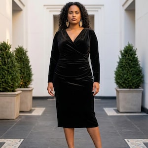 May include: A black velvet midi dress featuring long sleeves, a V-neckline, and a wrap-style bodice with gathered detailing at the waist. The dress has a fitted silhouette that falls below the knees, crafted from a soft, light-reflecting fabric.