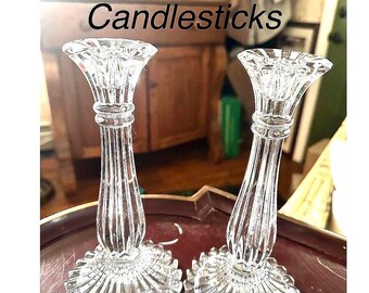 May include: Two clear crystal candlesticks with a fluted design. The candlesticks have a wide, scalloped base and a flared top. The text "Crystal Candlesticks" is visible in the image. These decorative candle holders are perfect for adding a touch of elegance to any room.