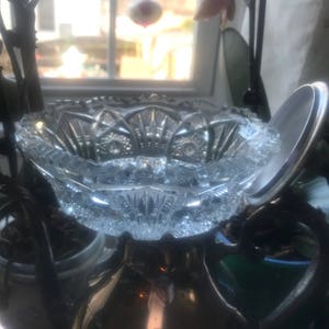 Puede incluir: Un cuenco de vidrio transparente con un dise&ntilde;o de vidrio cortado. El cuenco est&aacute; colocado encima de una jarra de plata.