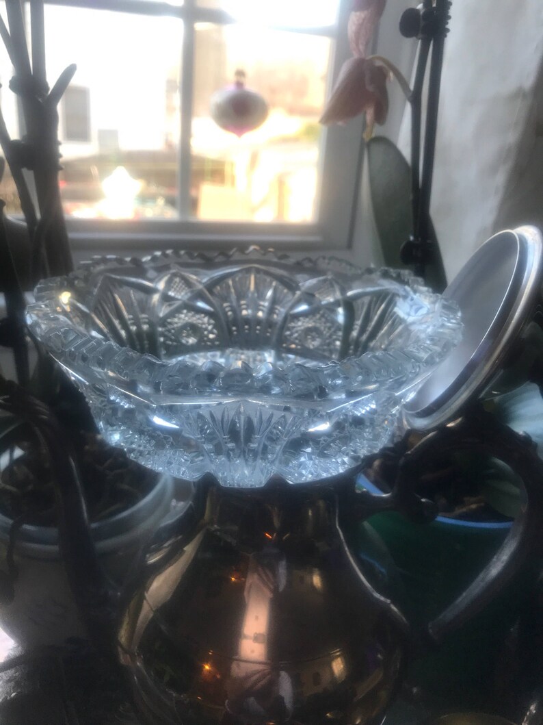 Puede incluir: Un cuenco de vidrio transparente con un dise&ntilde;o de vidrio cortado. El cuenco est&aacute; colocado encima de una jarra de plata.